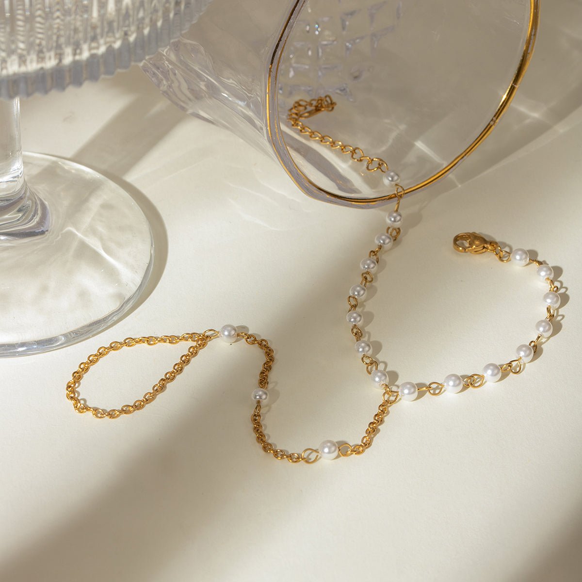 Gold and pearl necklace on a beige surface with a glass object in the background