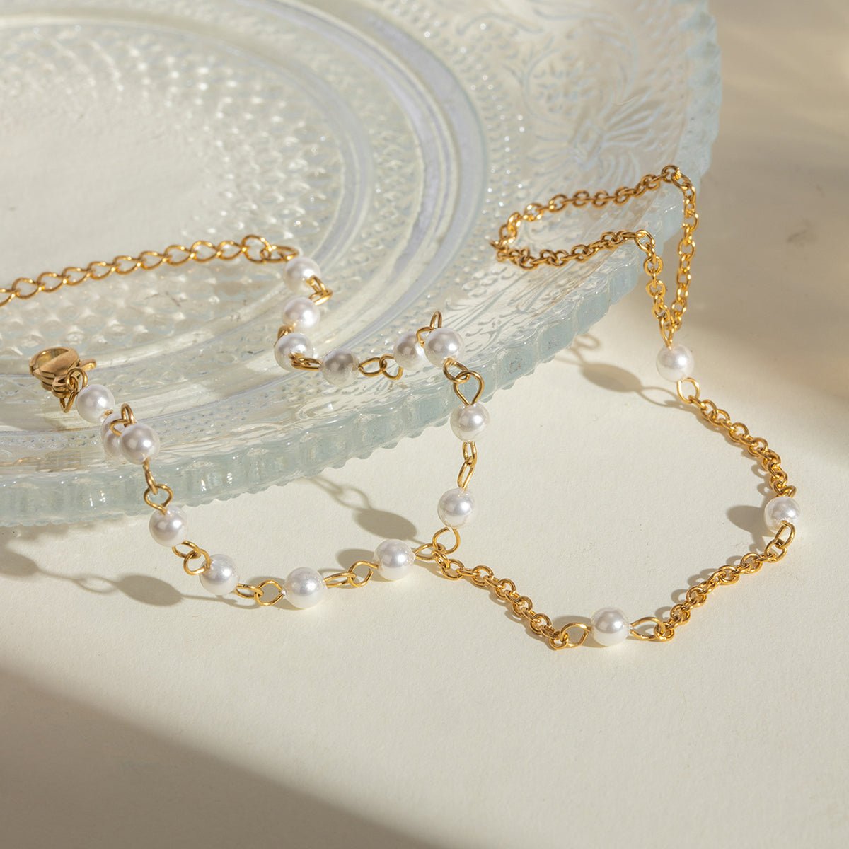 Gold chain and pearl necklace on a textured white surface