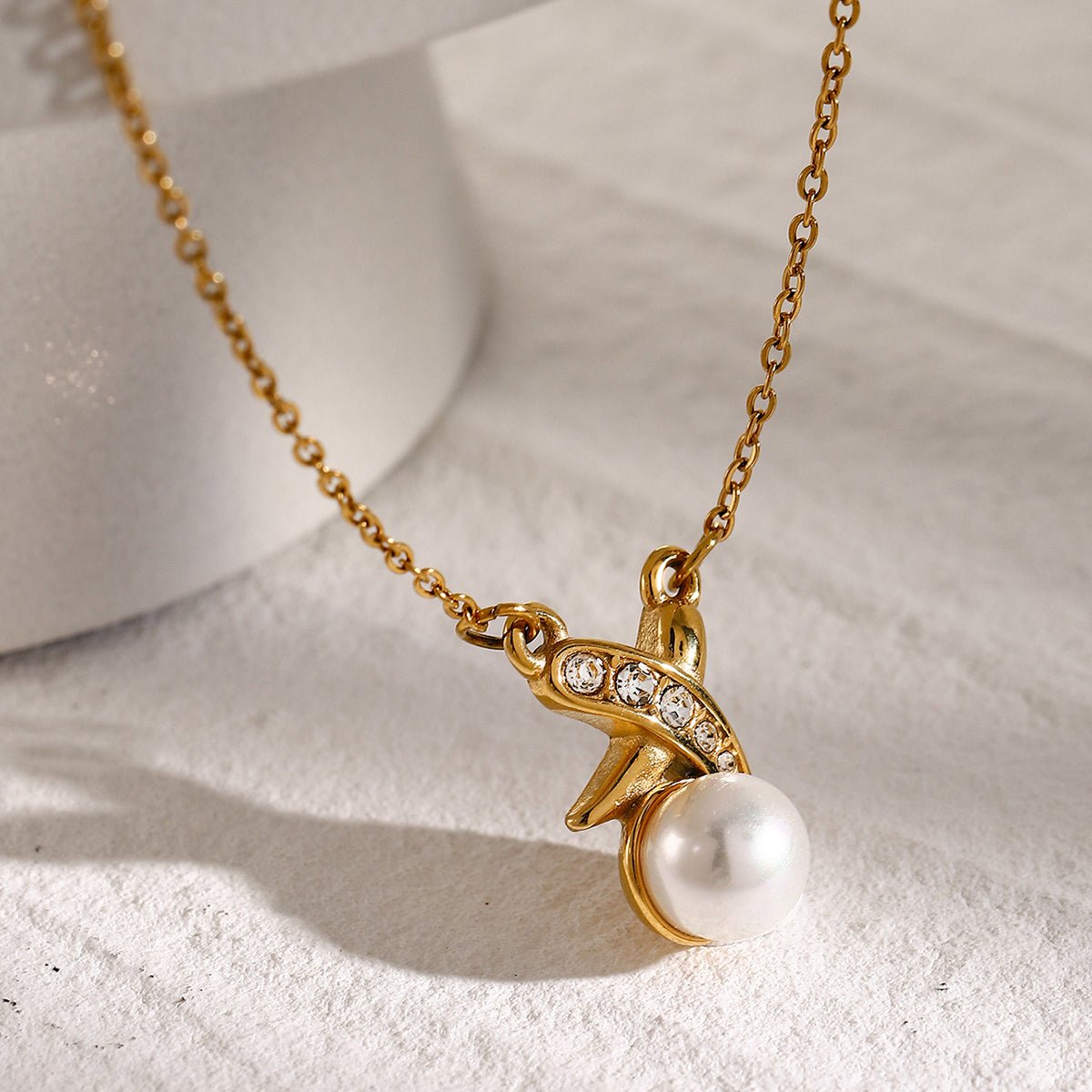 Gold necklace with a pearl pendant on a textured surface