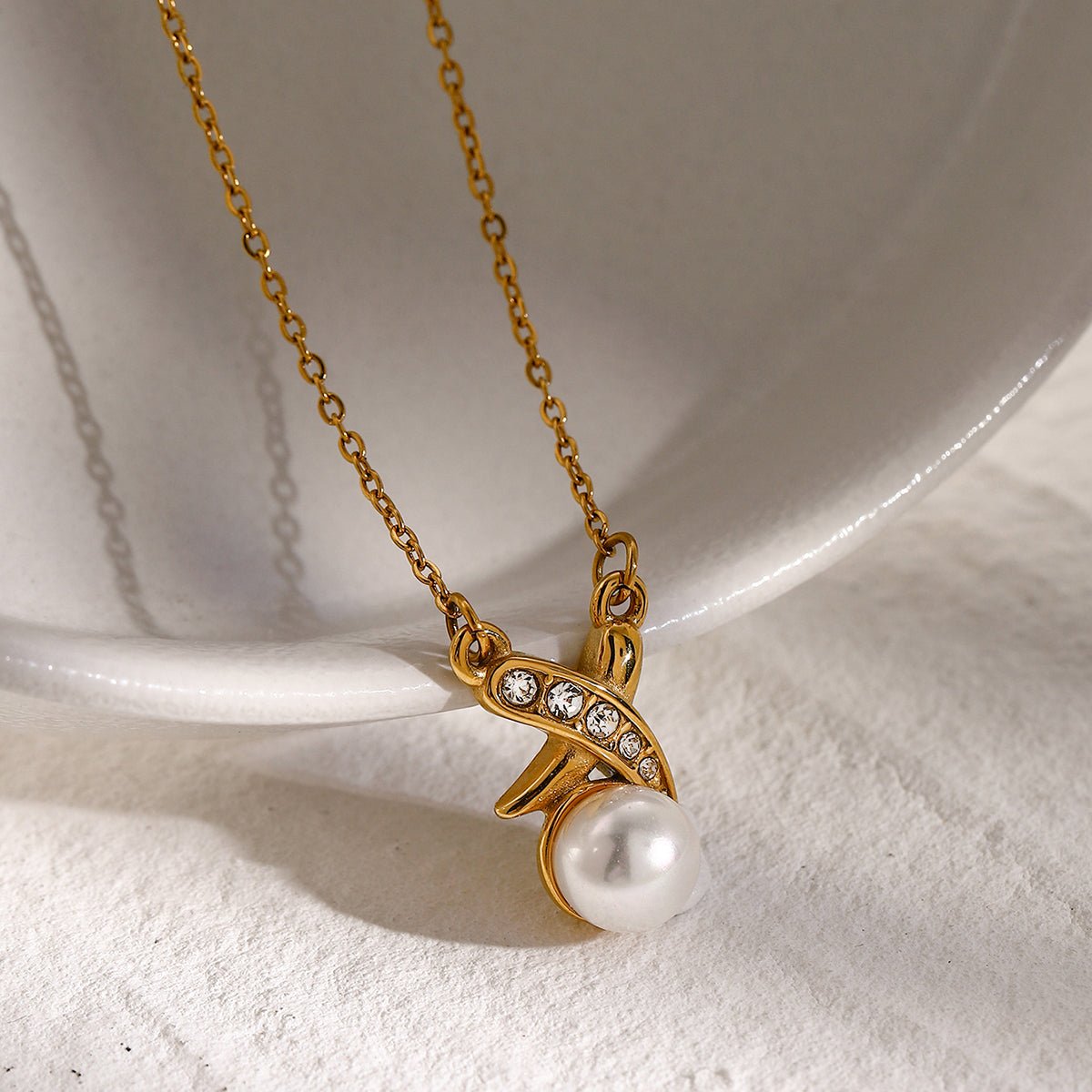 Gold necklace with a pendant featuring a pearl and small diamonds on a white background