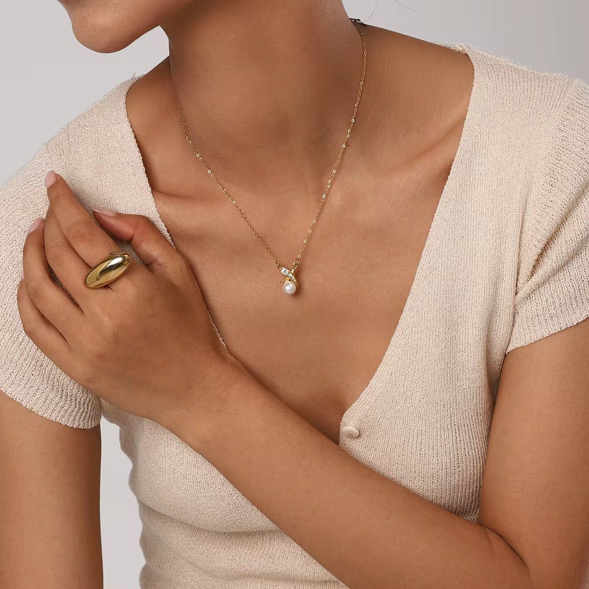 Woman wearing a gold necklace with a pearl pendant and a gold ring on a neutral background