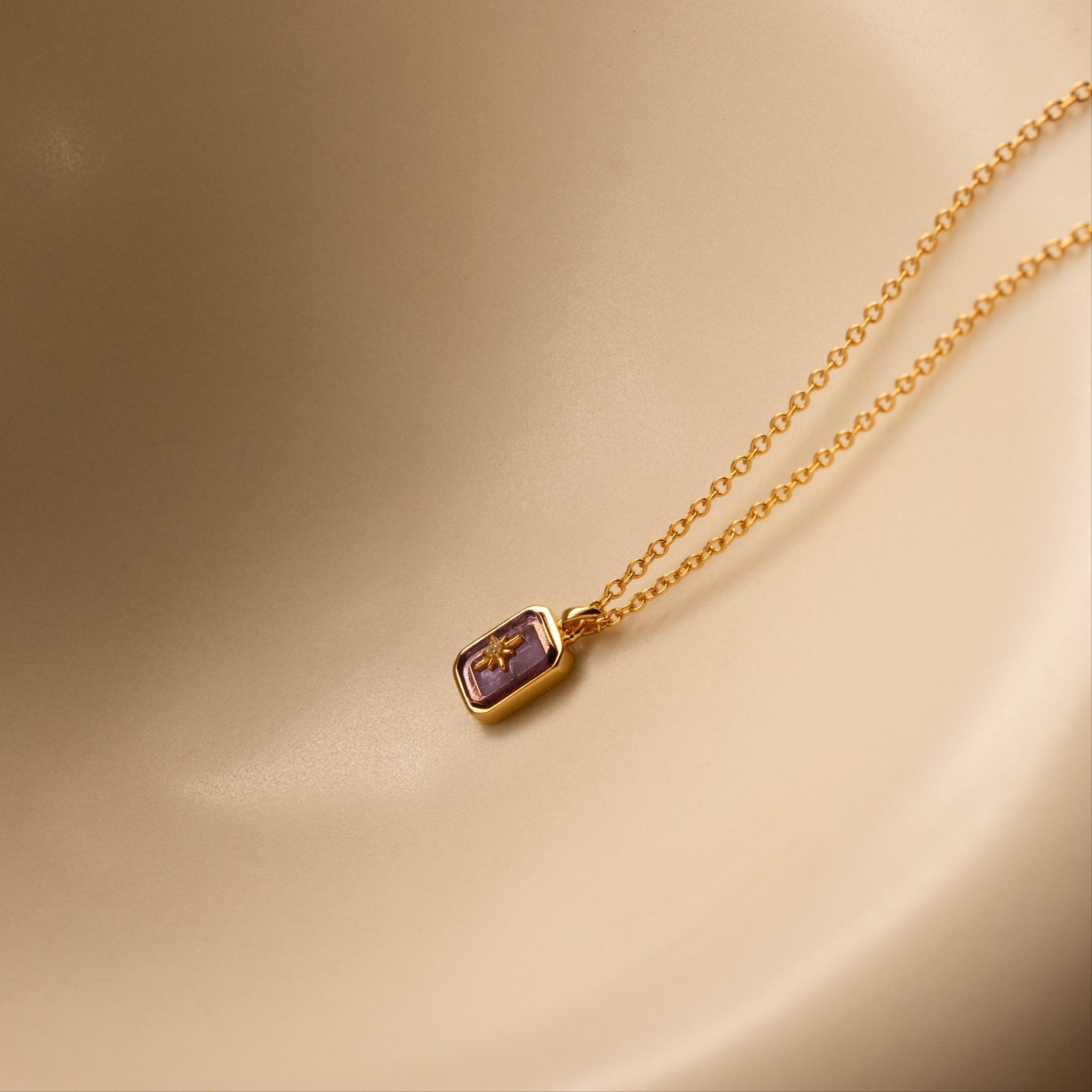 Gold necklace with a purple gemstone pendant on a beige background