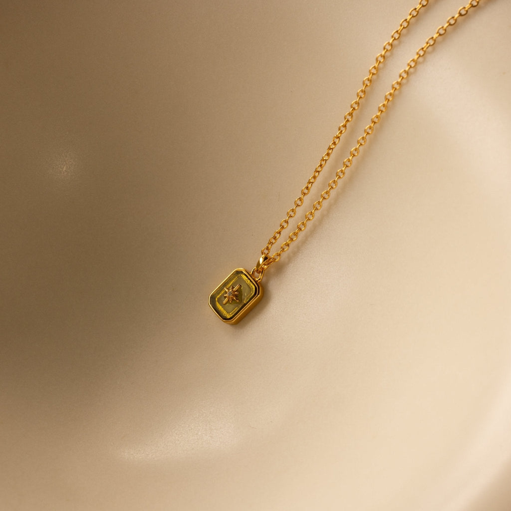 Gold necklace with a square pendant on a beige background