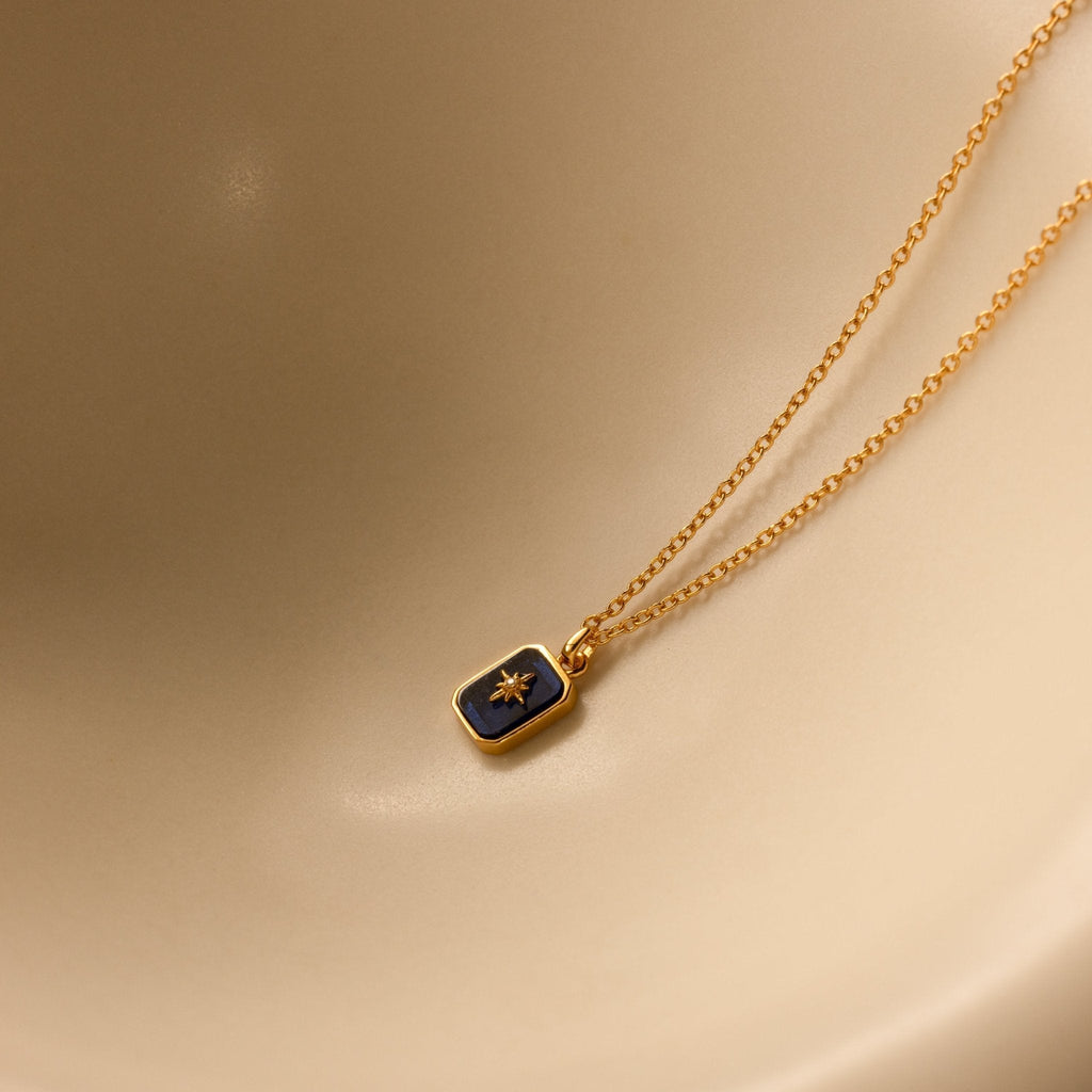 Gold necklace with a blue pendant on a beige background