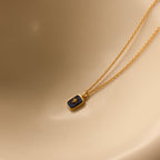 Gold necklace with a blue pendant on a beige background