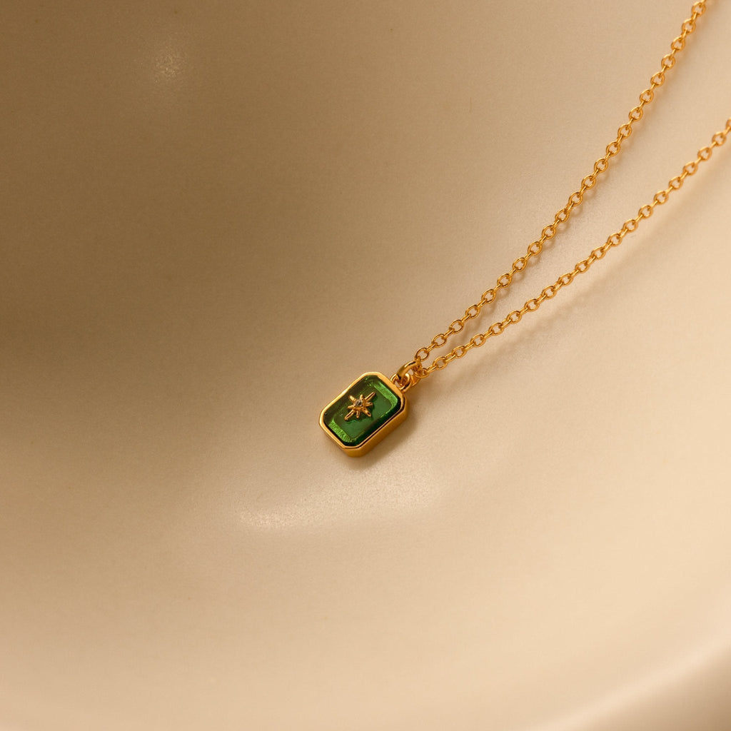 Gold necklace with a green pendant on a beige background