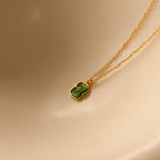Gold necklace with a green pendant on a beige background