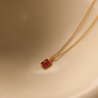 Gold necklace with a red pendant on a beige background