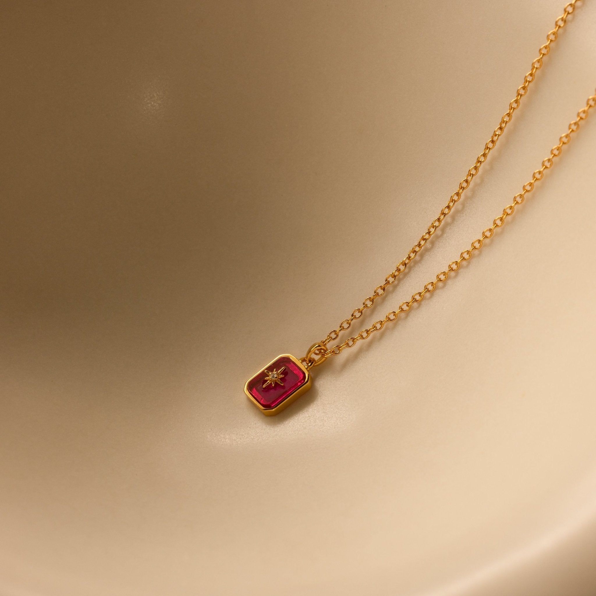 Gold necklace with a red pendant on a beige background