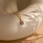 Gold necklace with a purple pendant on a beige surface