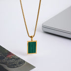 Gold necklace with a green square pendant on a white surface