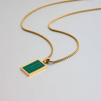Gold necklace with a green pendant on a light gray background