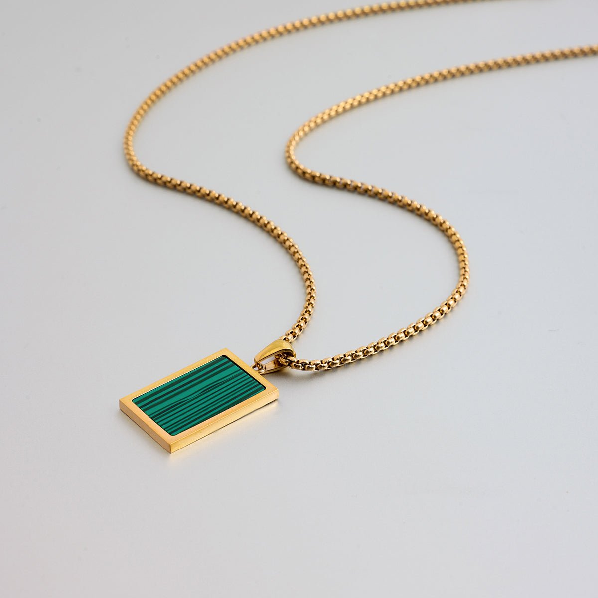 Gold necklace with a green pendant on a light gray background