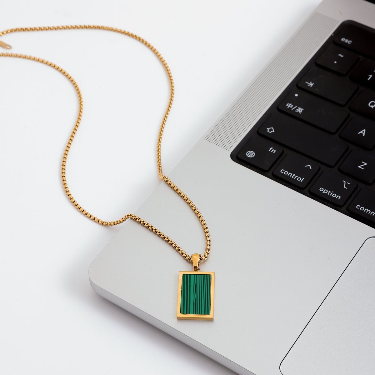Gold necklace with a green pendant on a laptop