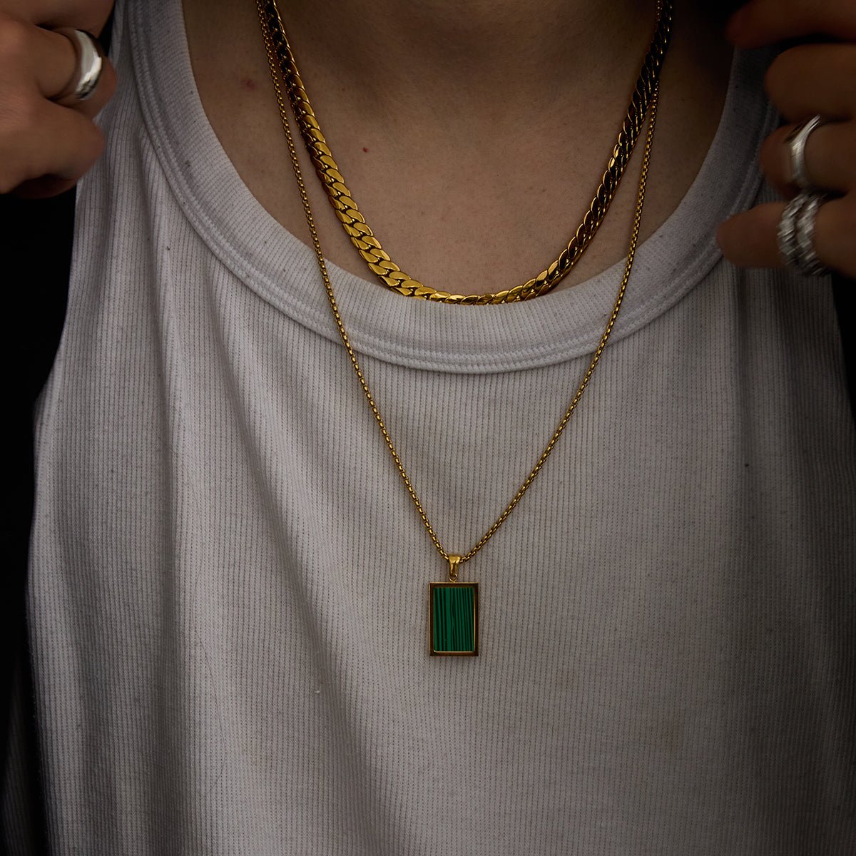 Person wearing a gold chain necklace with a green pendant on a plain background