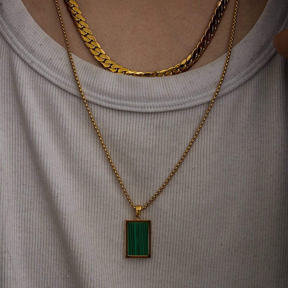Gold necklace with a green pendant on a light gray background