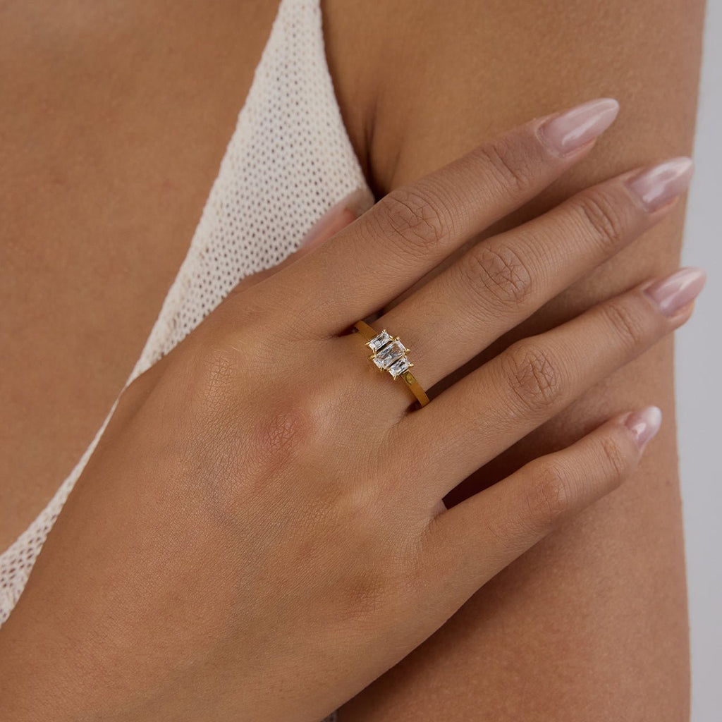 Hand wearing a gold ring with a diamond on a neutral background