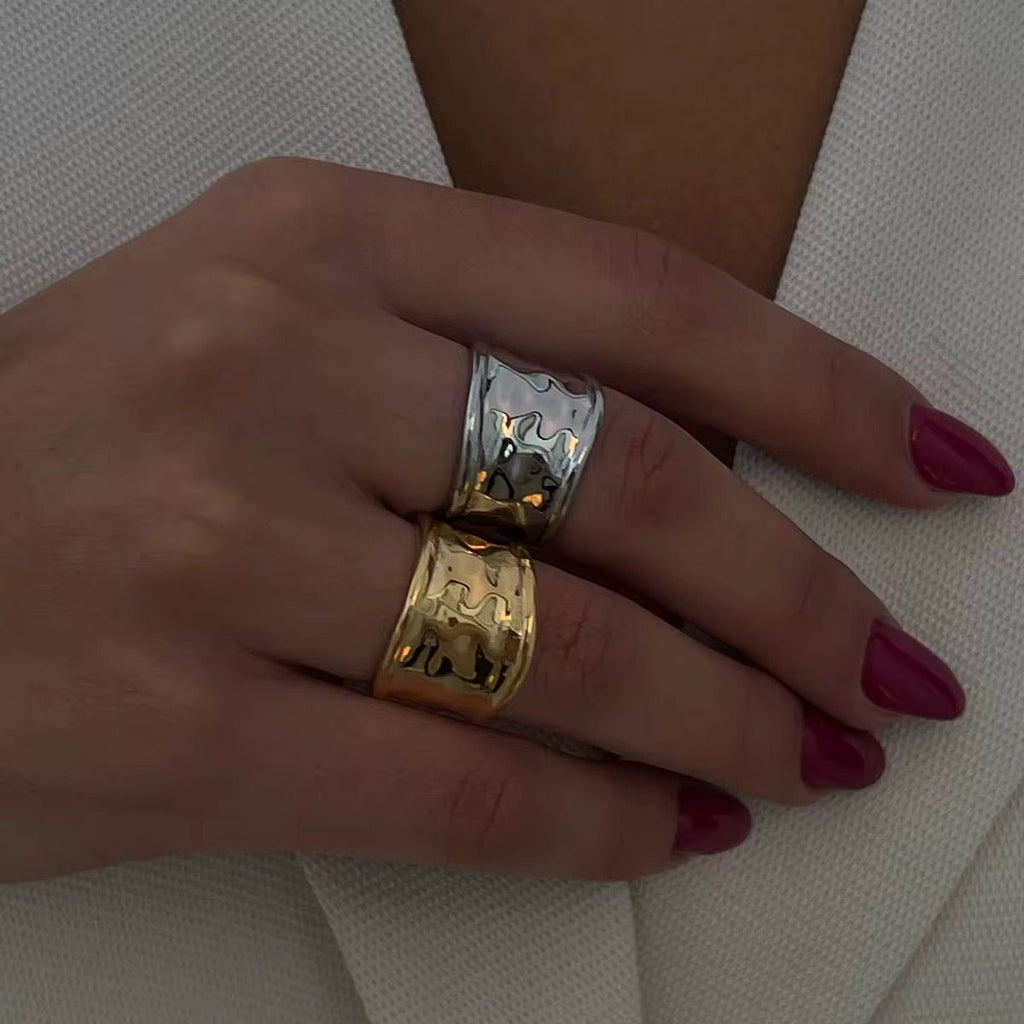 Hand wearing two rings, one gold and one silver, on a neutral background