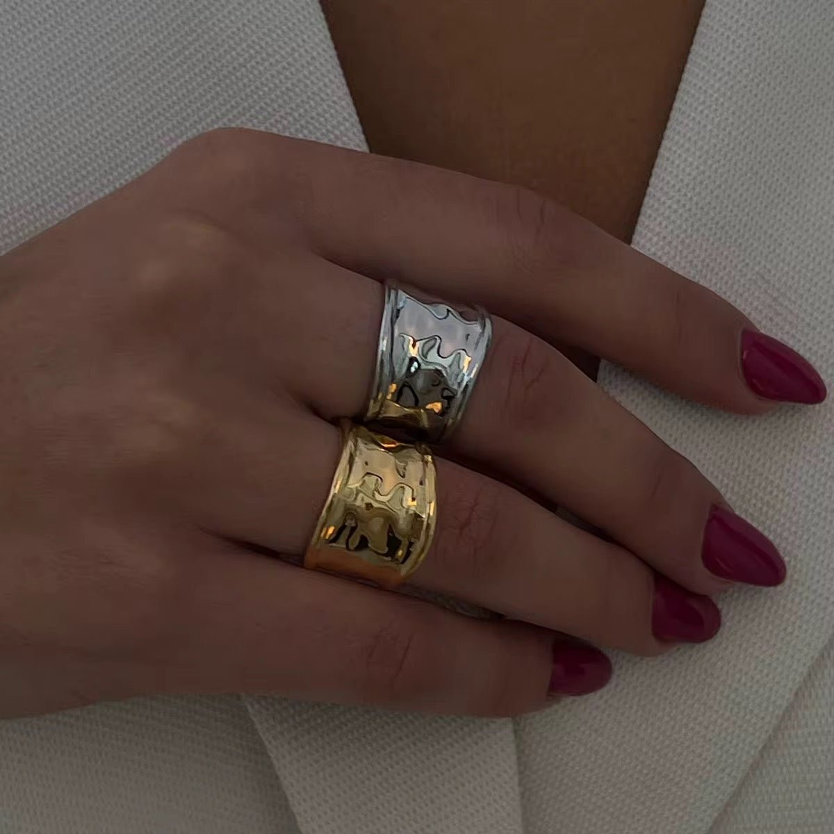 Hand wearing two rings, one gold and one silver, on a neutral background