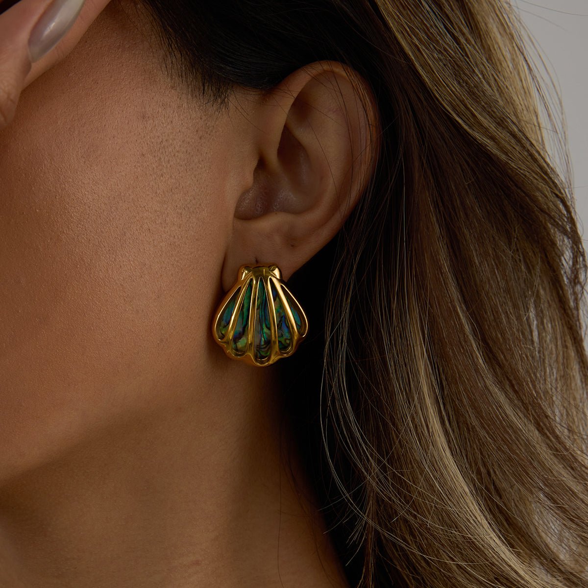Gold and green earrings worn by a person with long hair.