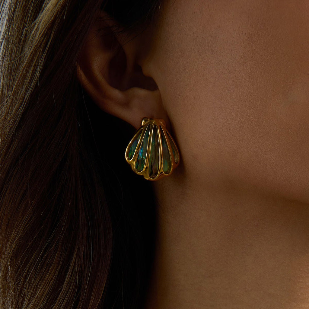 Gold shell-shaped earring worn by a person with dark hair.