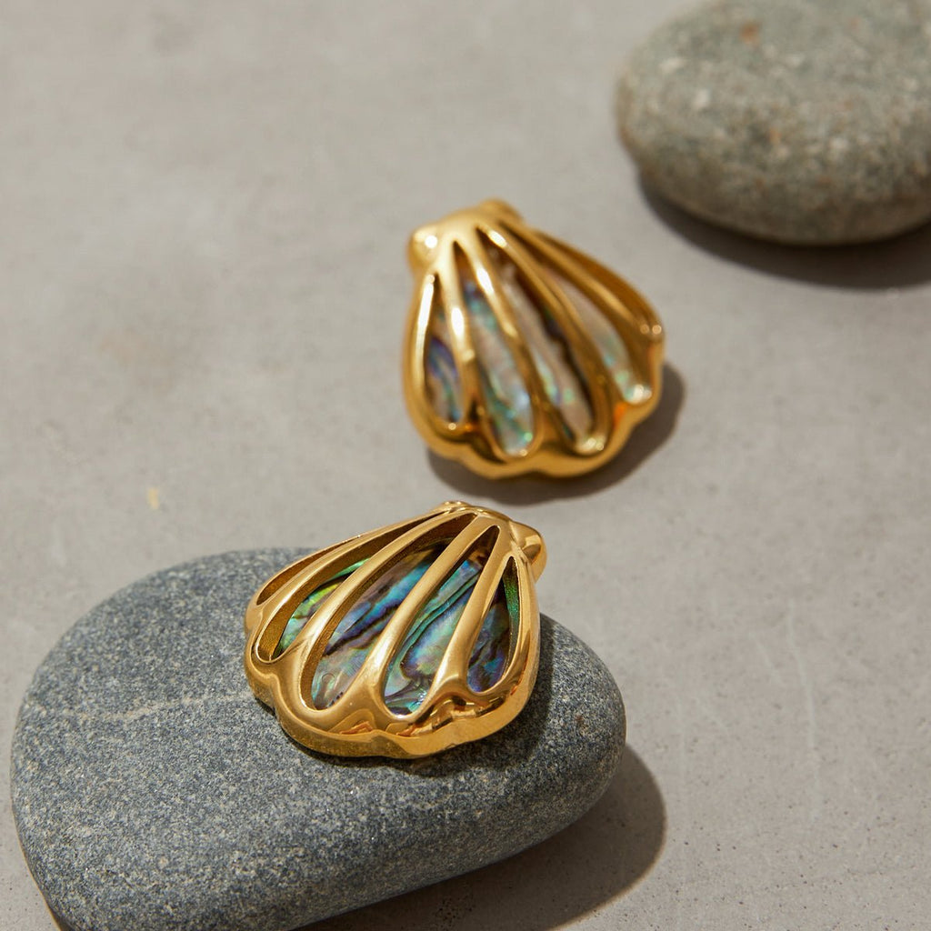 Gold shell-shaped earrings with abalone interior on a stone surface
