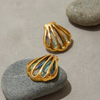 Gold shell-shaped earrings with abalone interior on a stone surface