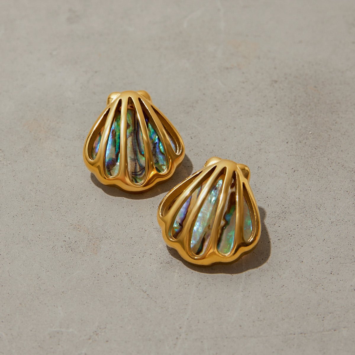 Gold shell-shaped earrings with multicolored stone inlays on a beige background