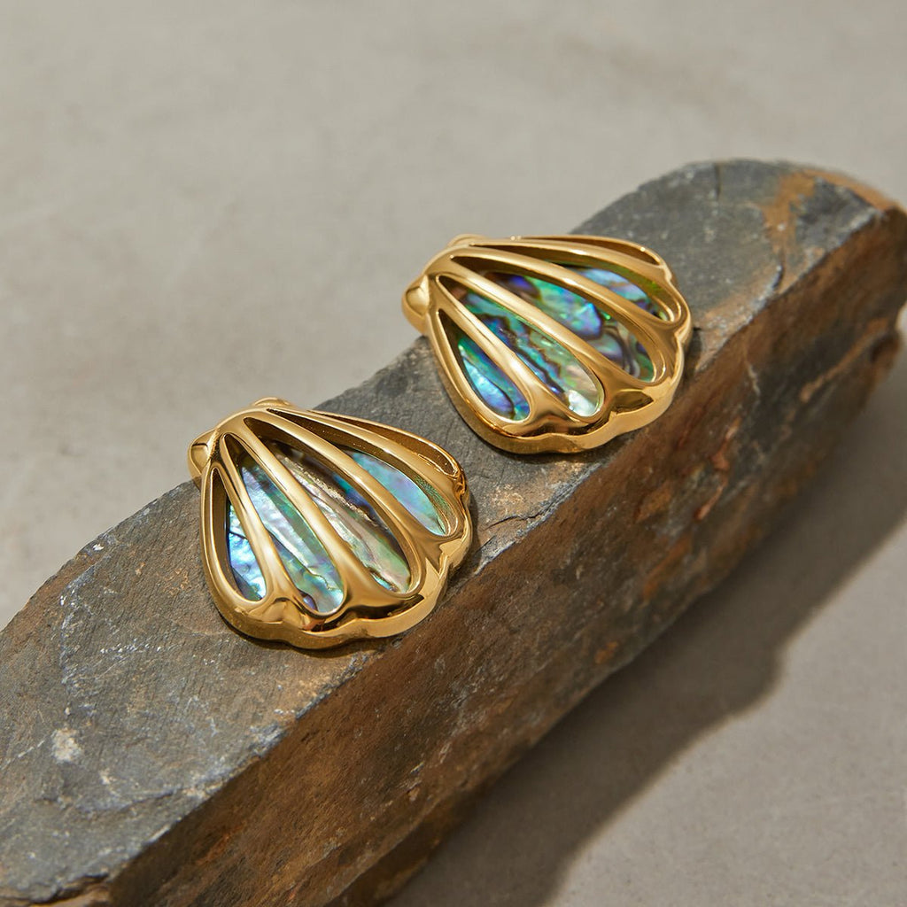 Gold shell-shaped earrings with iridescent center on a stone surface