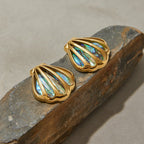 Gold shell-shaped earrings with iridescent center on a stone surface