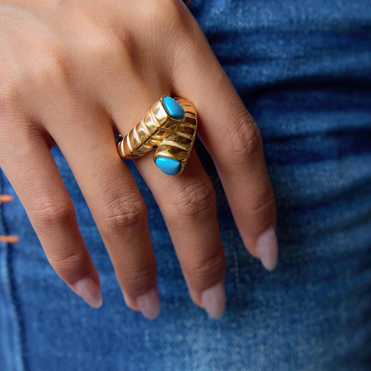Hand wearing a gold ring with blue stones against a blue denim background