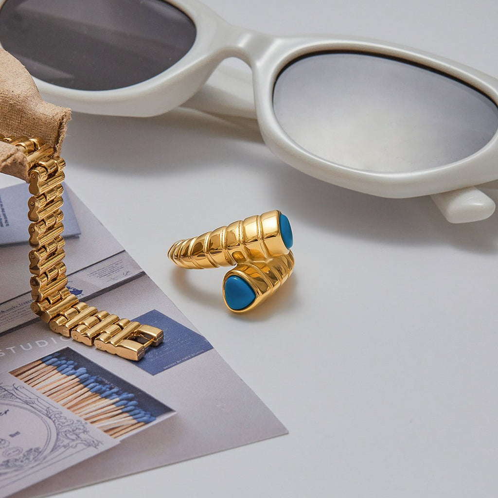 Gold bracelet and ring with blue stones on a surface with sunglasses in the background