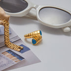 Gold bracelet and ring with blue stones on a surface with sunglasses in the background