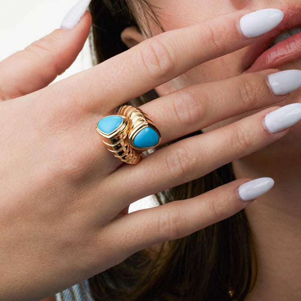 Gold ring with blue stones on a hand with white nail polish