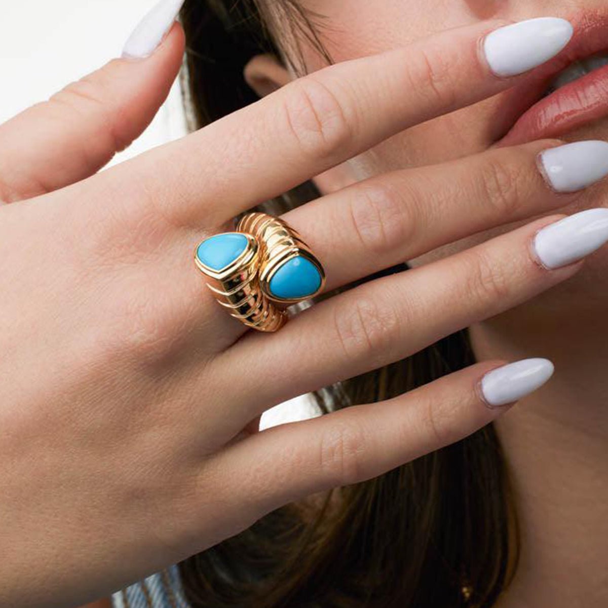 Gold ring with blue stones on a hand with white nail polish