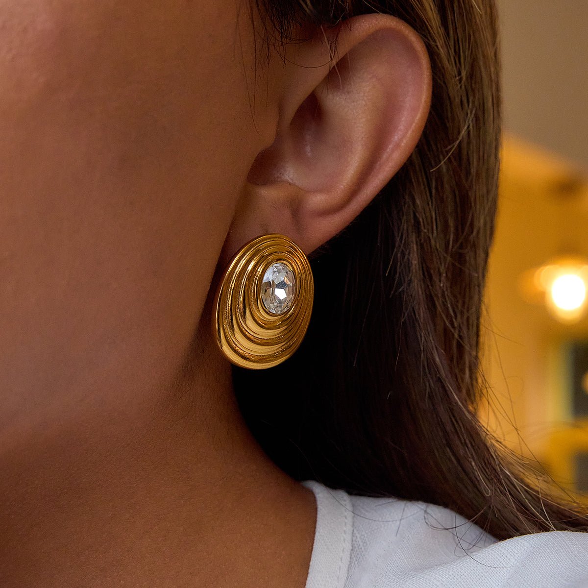 Close-up of a gold earring with a clear gemstone worn by a person. Statement stud earrings with spiral design in gold


