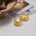 Gold earrings on a white surface with a magazine in the background