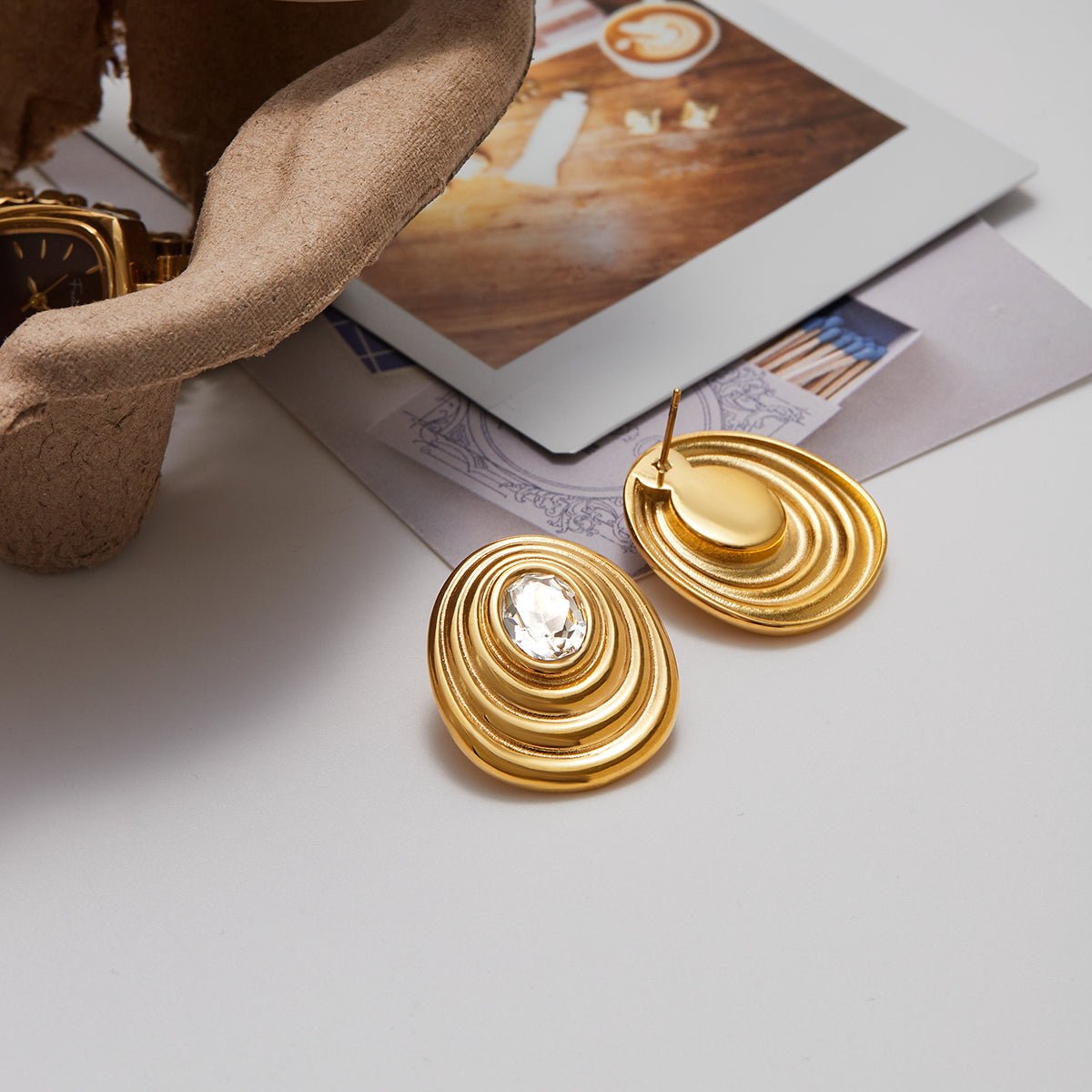 Gold earrings on a white surface with a magazine in the background