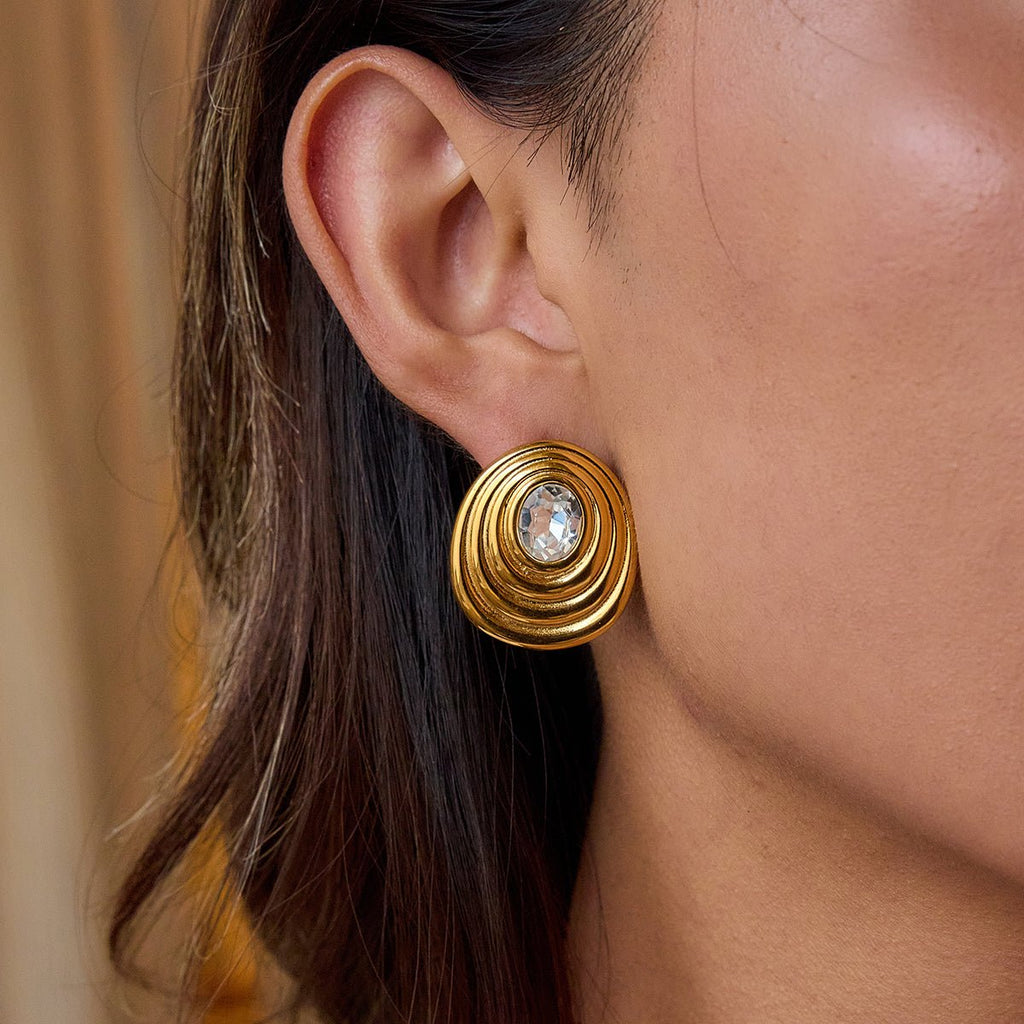 Gold earring with a central gemstone worn by a person.18K gold ripple stud earrings with gemstone center

