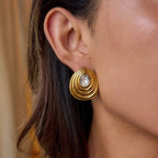Gold earring with a central gemstone worn by a person.18K gold ripple stud earrings with gemstone center

