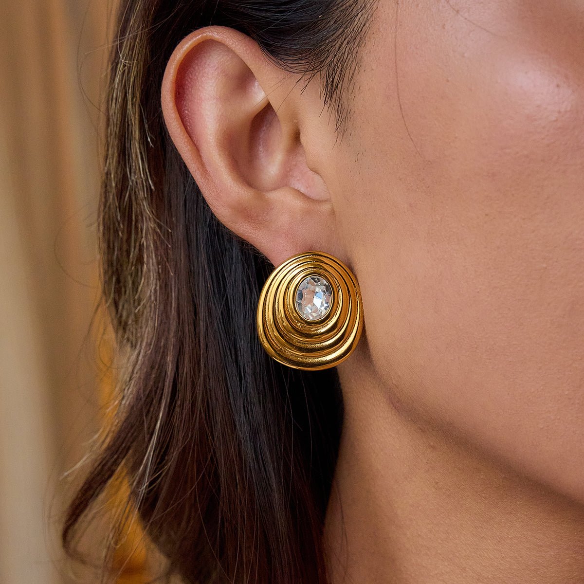 Gold earring with a central gemstone worn by a person.18K gold ripple stud earrings with gemstone center

