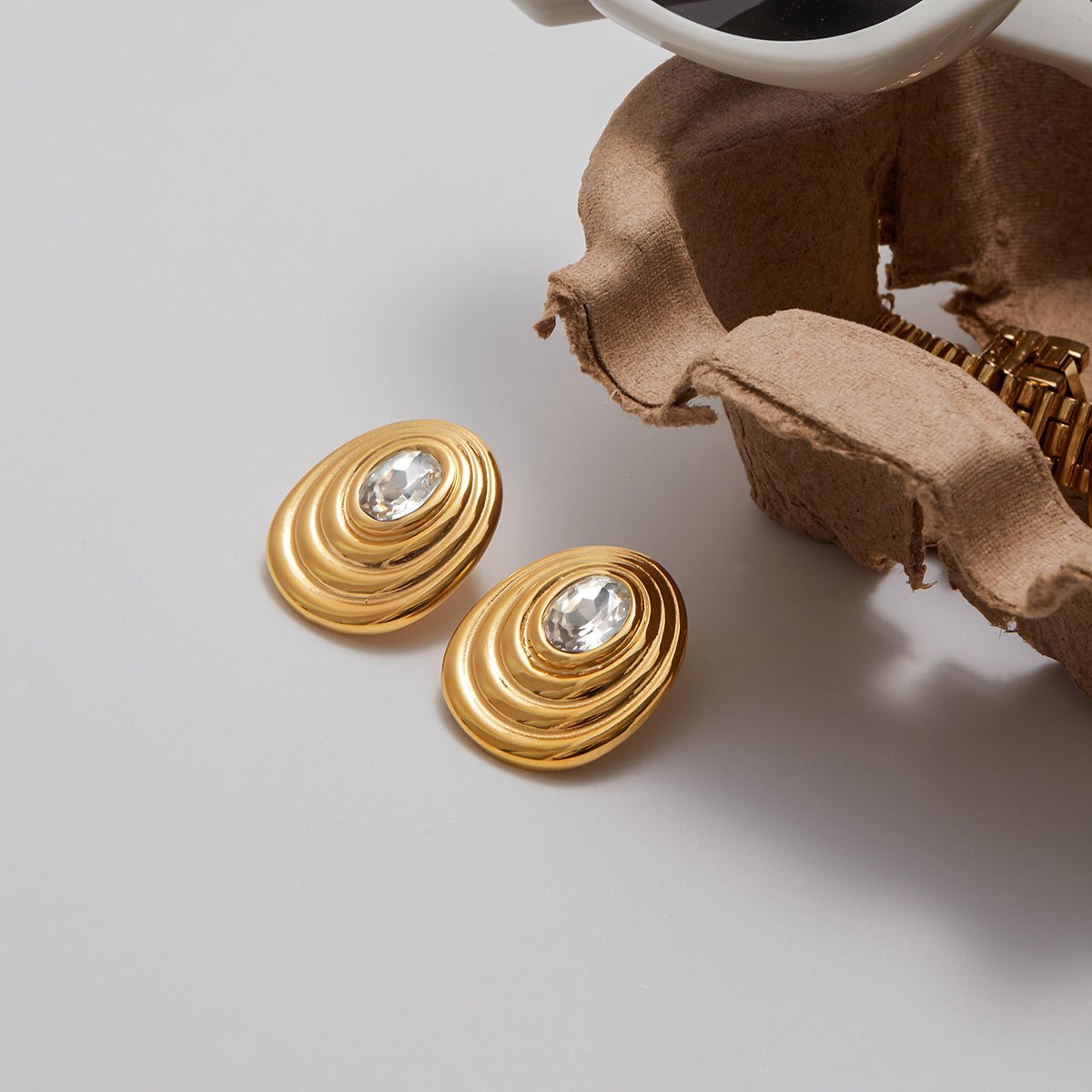 Gold earrings with a central gemstone on a light gray background Modern gold spiral earrings for women

