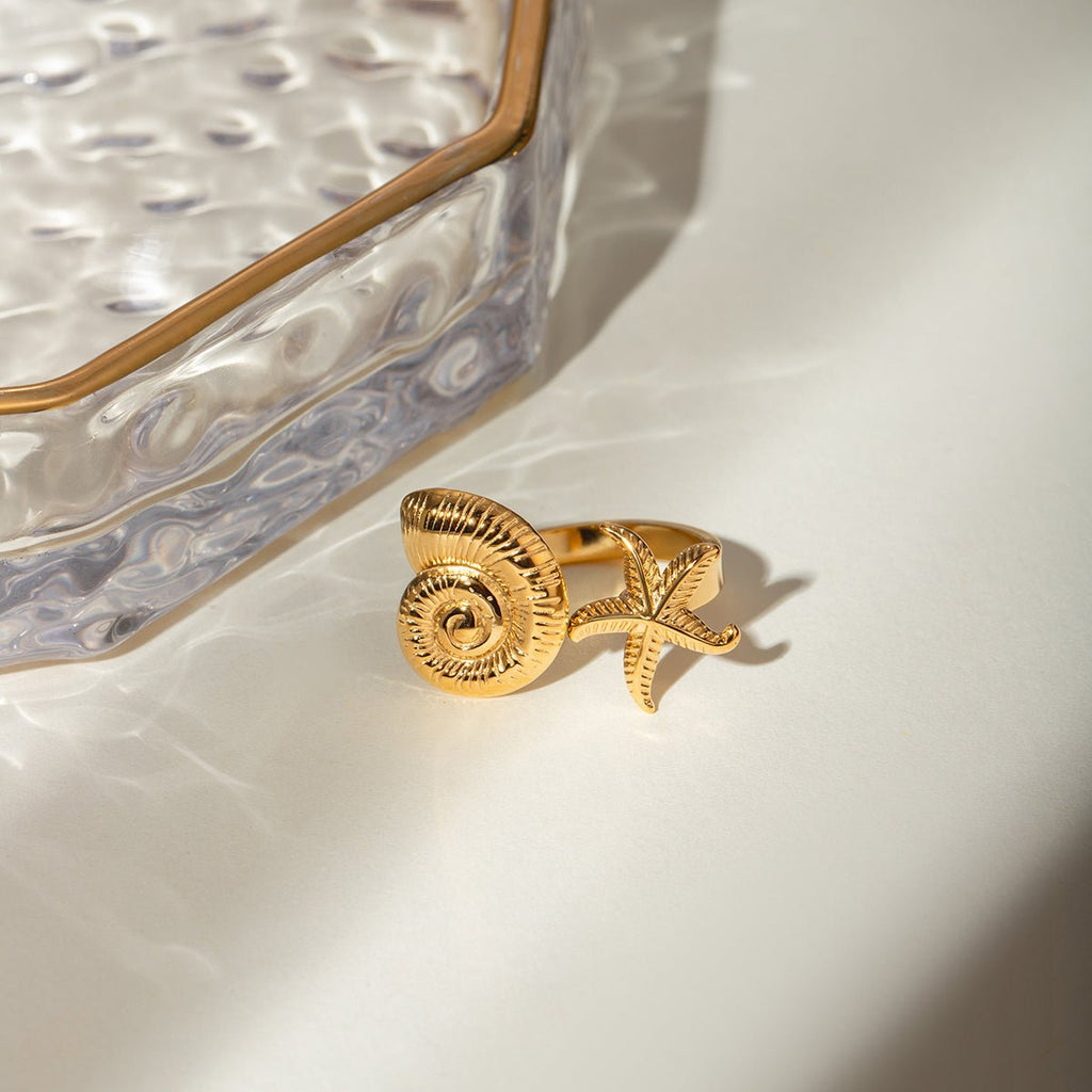 Gold ring with shell and starfish design on a white surface