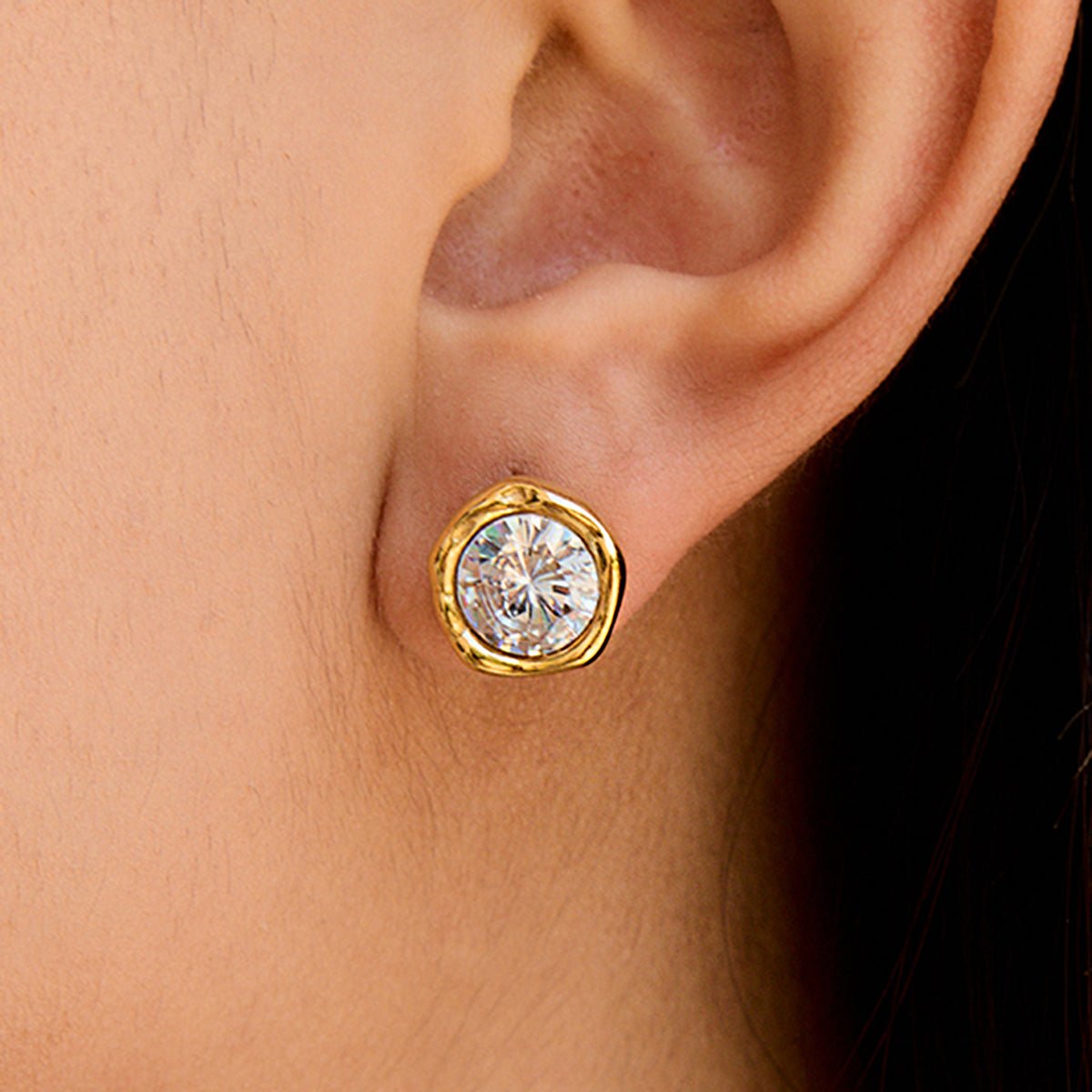 Gold earring with a clear gemstone worn on an ear