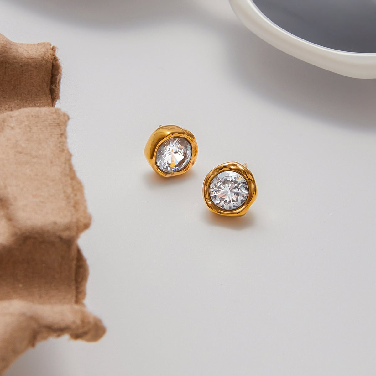 Gold earrings with clear gemstones on a light surface