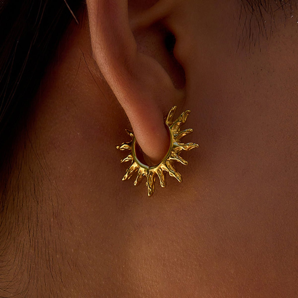 Gold sun-shaped earring worn on an ear with a close-up view.
