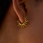 Gold sun-shaped earring worn on an ear with a close-up view.