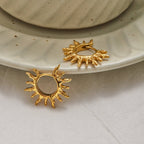 Gold sun-shaped earrings on a textured white surface