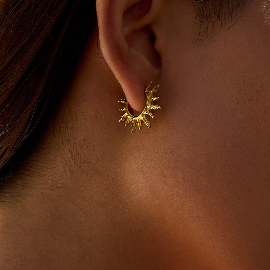 Gold earring worn on an ear with a blurred background