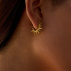 Gold earring worn on an ear with a blurred background